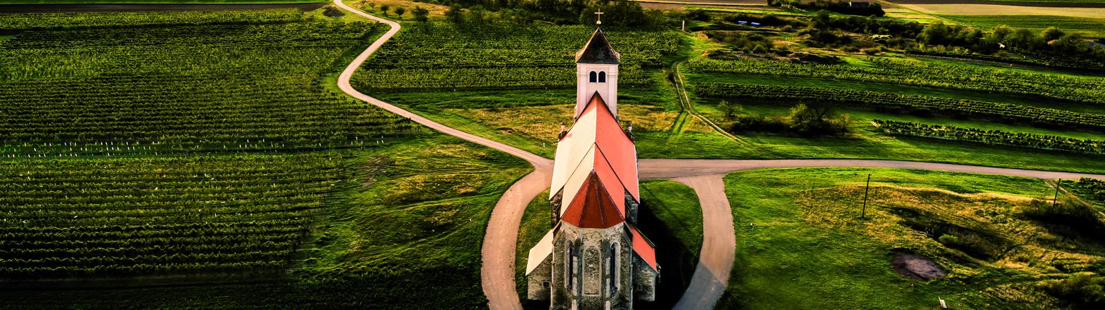 Blick aus der Vogelperspektive auf eine kleine Kirche am Wartberg umgeben von grünen Feldern