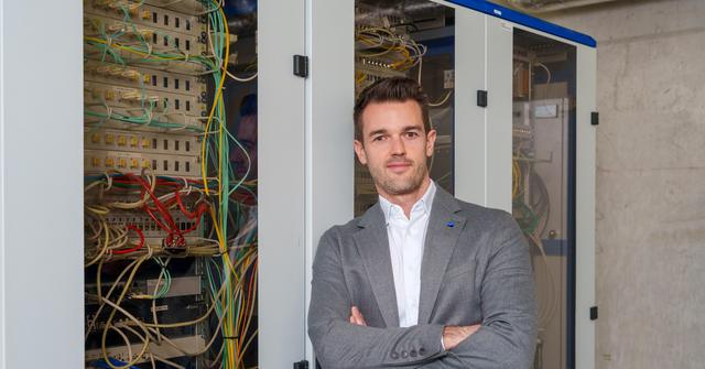 Mann mittleren Alters mit weißem Hemd und grauem Anzug lehnt an einem Serverschrank.