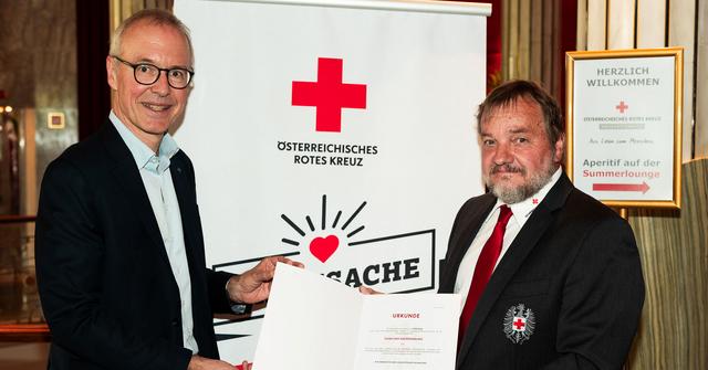 Zwei Männer in Anzug und Krawatte halten eine Urkunde.