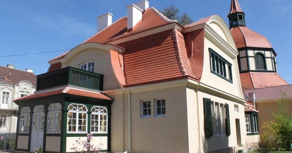 gelbes Gebäude mit grünen Fensterläden und großer roter Dachfläche inkl. Dachkuppel