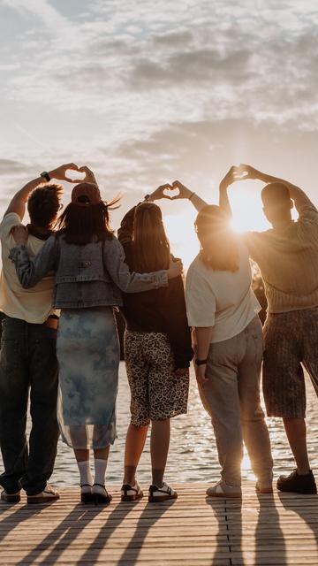 Jugendliche formen ihre Hände zu Herzen und blicken in den Sonnenuntergang