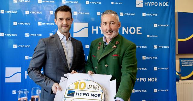 2 Männern und 2 Frauen steht vor einer blauen Wand mit Aufschrift "HYPO NOE" und halten eine Torte in die Kamera.