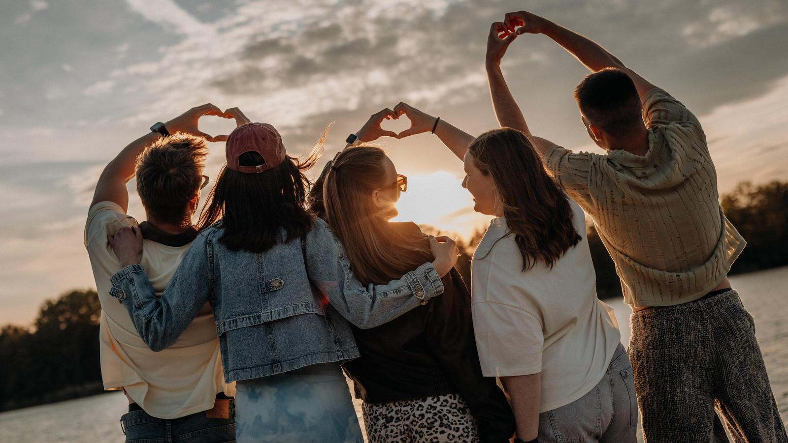Jugendliche formen Handherzen und blicken in den Sonnenuntergang