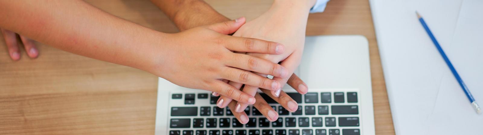 Drei Personen in Business-Kleidung legen ihre Hände übereinander.